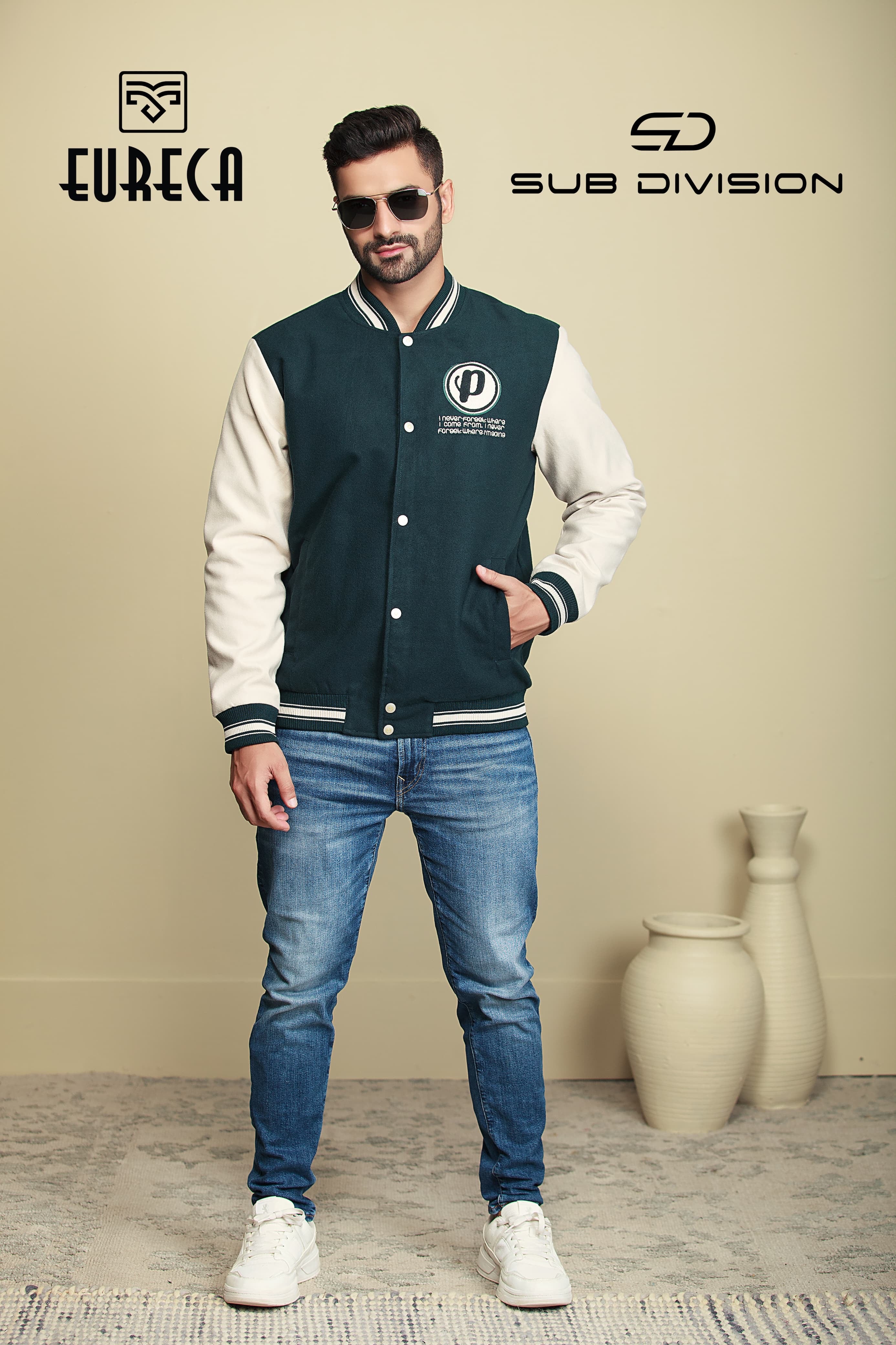 Man wearing a varsity jacket with visible branding with embroidery philosophy against a beige wall.