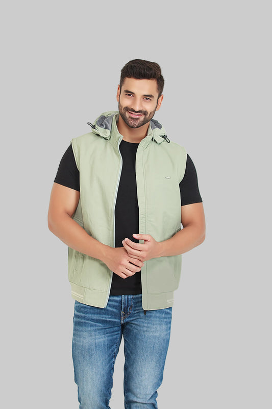 Man wearing a light green vest over a black shirt with blue jeans on a gray background